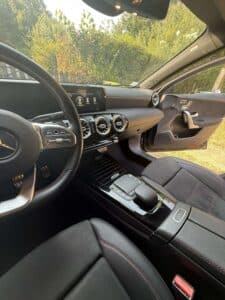 Vue intérieure Mercedes Classe A : volant cuir rouge, écran MBUX, commandes tactiles, sièges noirs et porte ouverte.