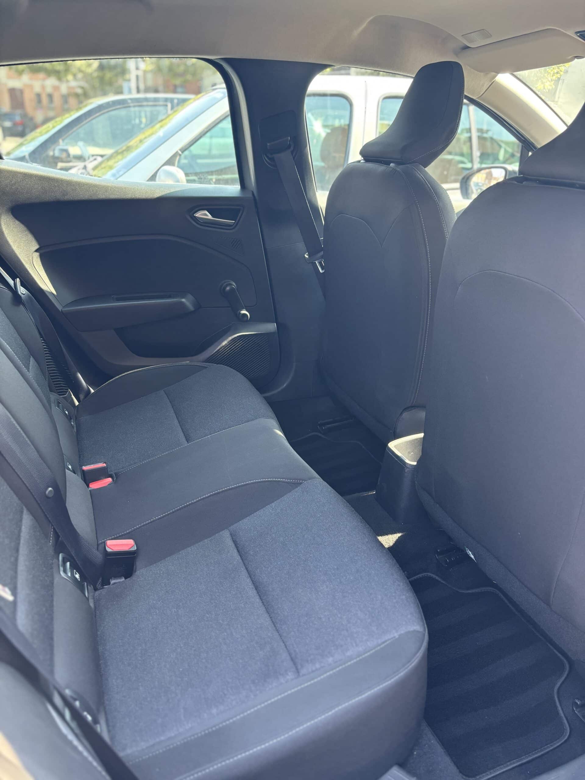 Intérieur de voiture vue arrière avec sièges tissus bleu-gris, boucles de ceinture rouges, et vue sur l'extérieur ensoleillé.