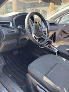 Intérieur conducteur Renault moderne : volant cuir siglé, tableau de bord digital, boutons d'aide à la conduite et siège en tissu.