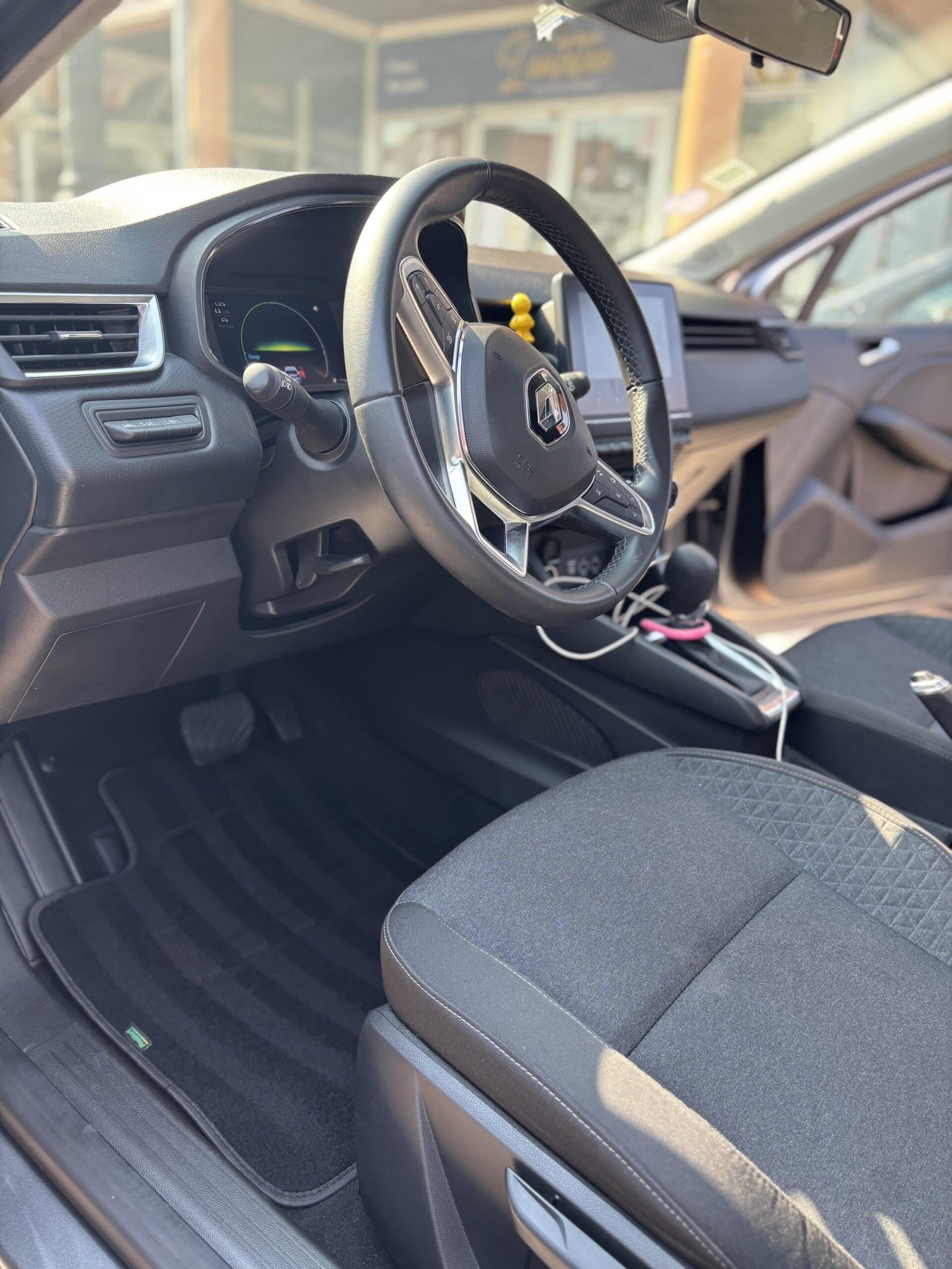 Intérieur conducteur Renault moderne : volant cuir siglé, tableau de bord digital, boutons d'aide à la conduite et siège en tissu.