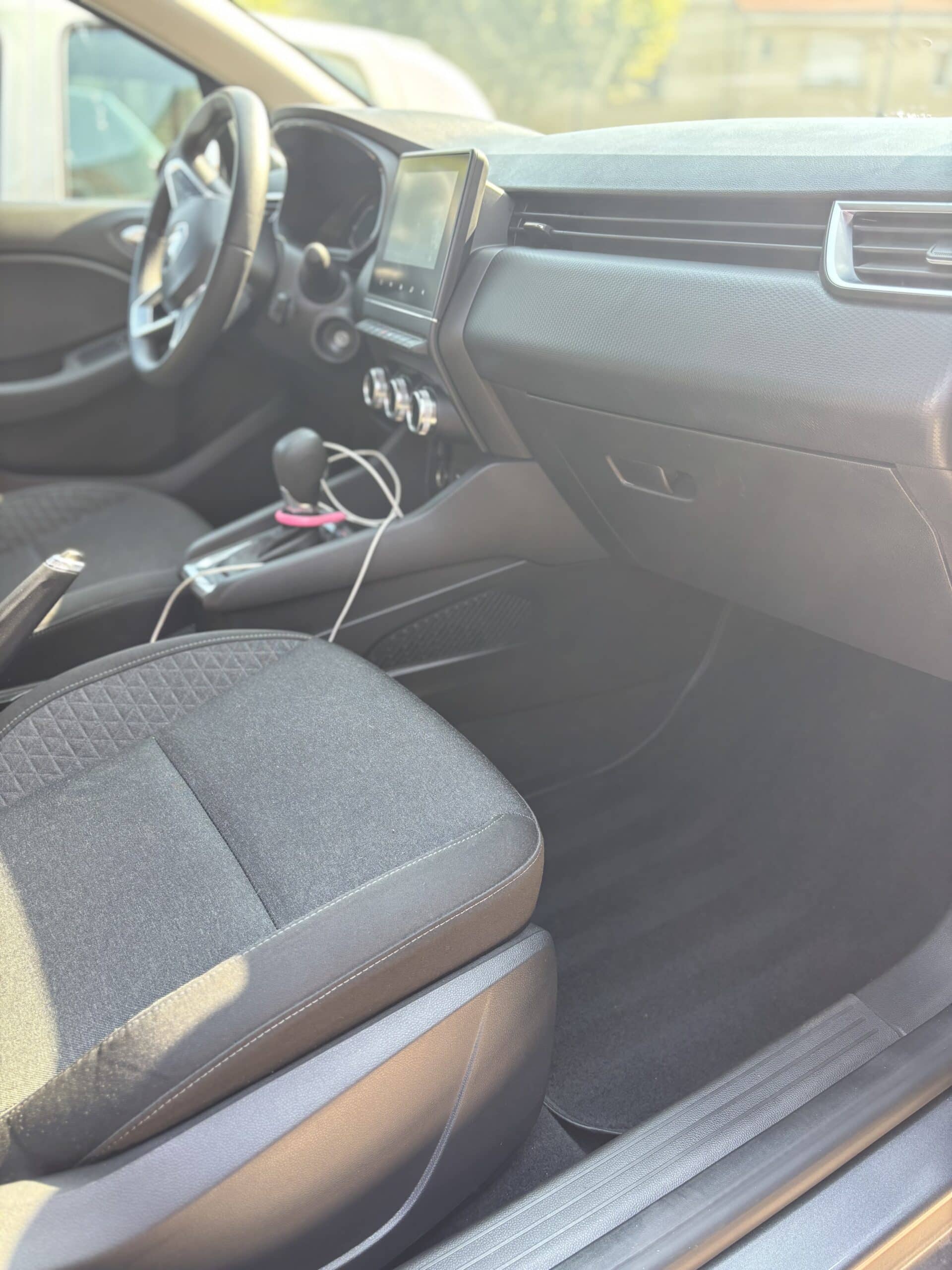Intérieur d'une voiture moderne, vue du siège passager avant, affichant le tableau de bord, écran tactile central, levier de vitesse et frein à main.