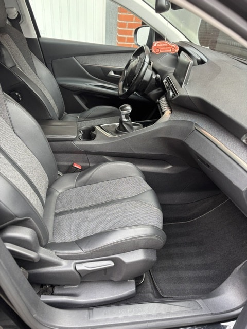 Intérieur Peugeot : Sièges, Boîte Manuelle et Ambiance Intérieur d'une Peugeot vue de côté passager : sièges cuir/tissu gris, levier de vitesses manuel, tableau de bord, et seuil de porte portant l'inscription PEUGEOT.