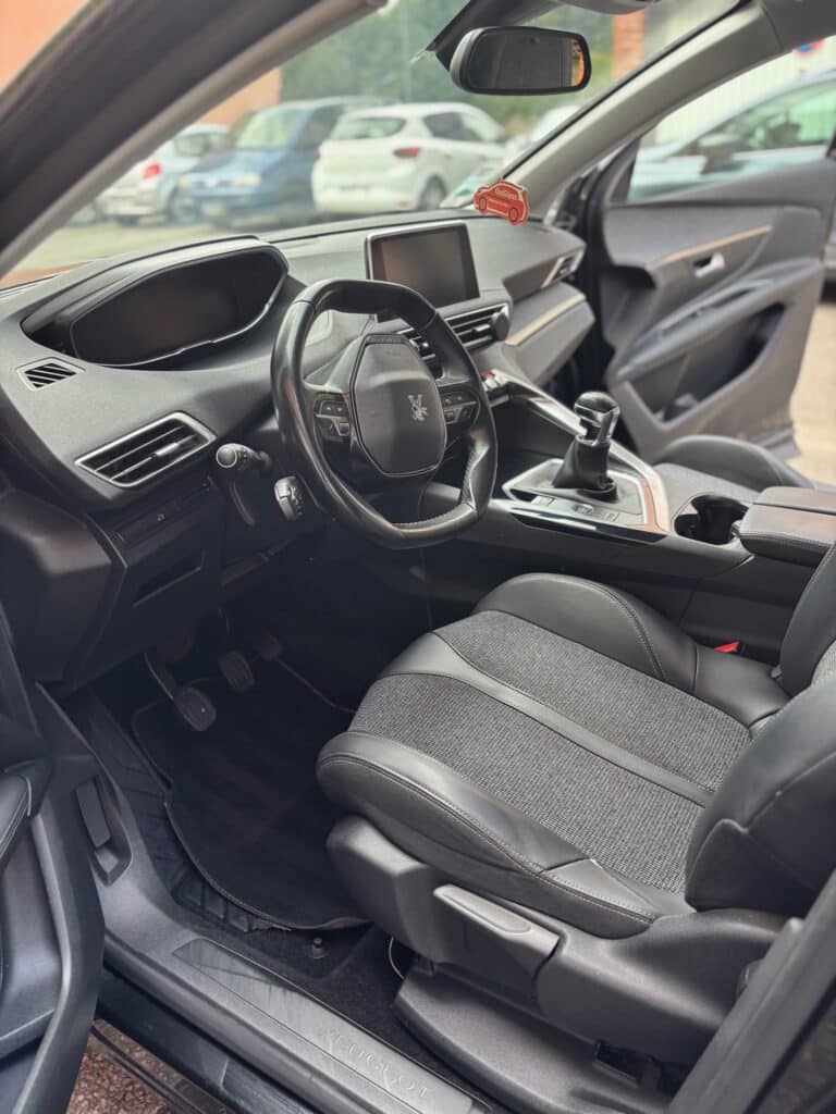 Intérieur Peugeot : Volant, Cockpit et Siège Intérieur conducteur Peugeot avec volant i-Cockpit, levier de vitesse automatique, sellerie tissu/cuir et pédalier, vue vers l'extérieur.