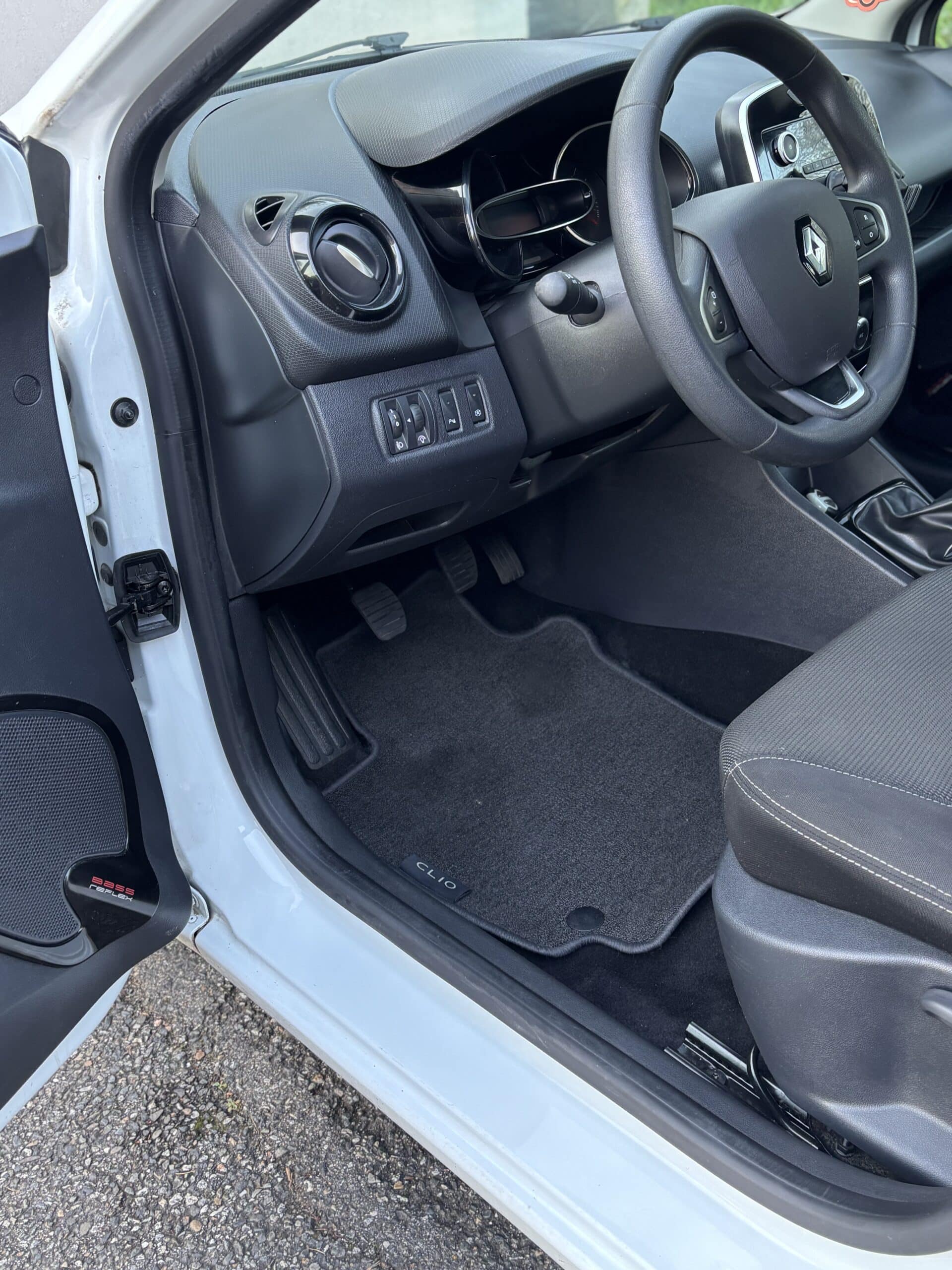 Intérieur d'une Renault Clio blanche montrant le volant, le tableau de bord et le tapis de sol marqué CLIO.