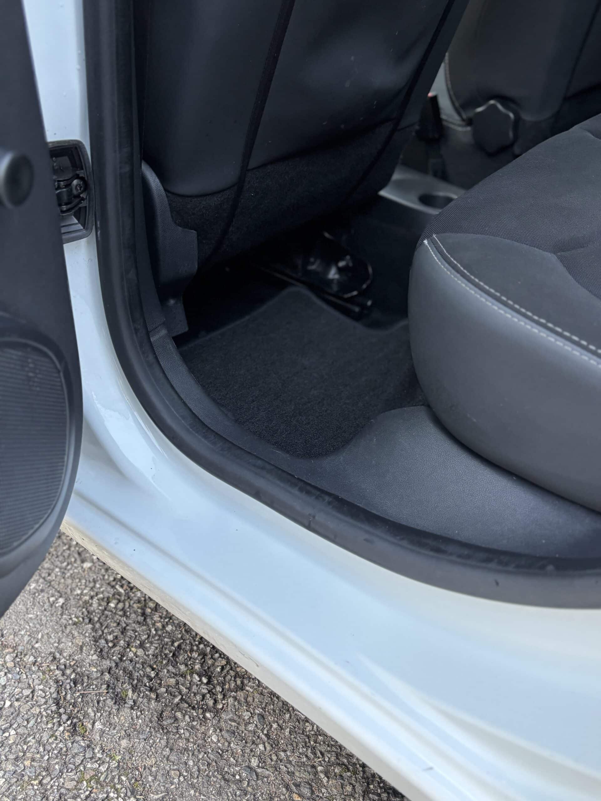 Intérieur d'une voiture blanche montrant un tapis de sol noir propre et le bas du siège passager arrière.