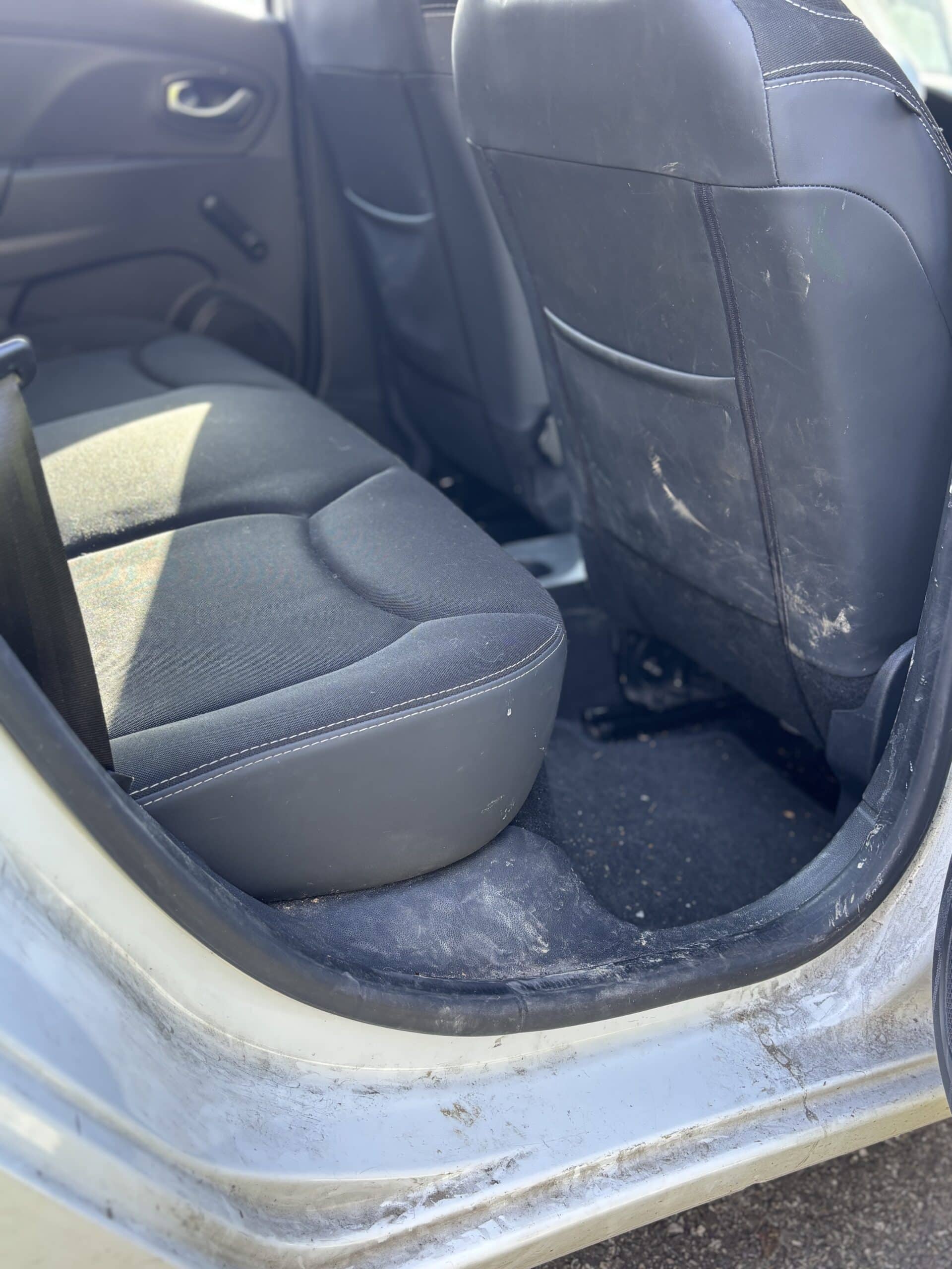 Intérieur de voiture sale avec siège arrière noir, tapis de sol poussiéreux et seuil de porte taché de boue.