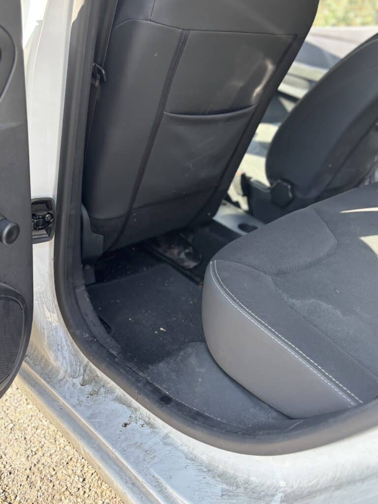 Intérieur de voiture blanche avec sièges noirs et tapis de sol sale nécessitant un nettoyage professionnel.