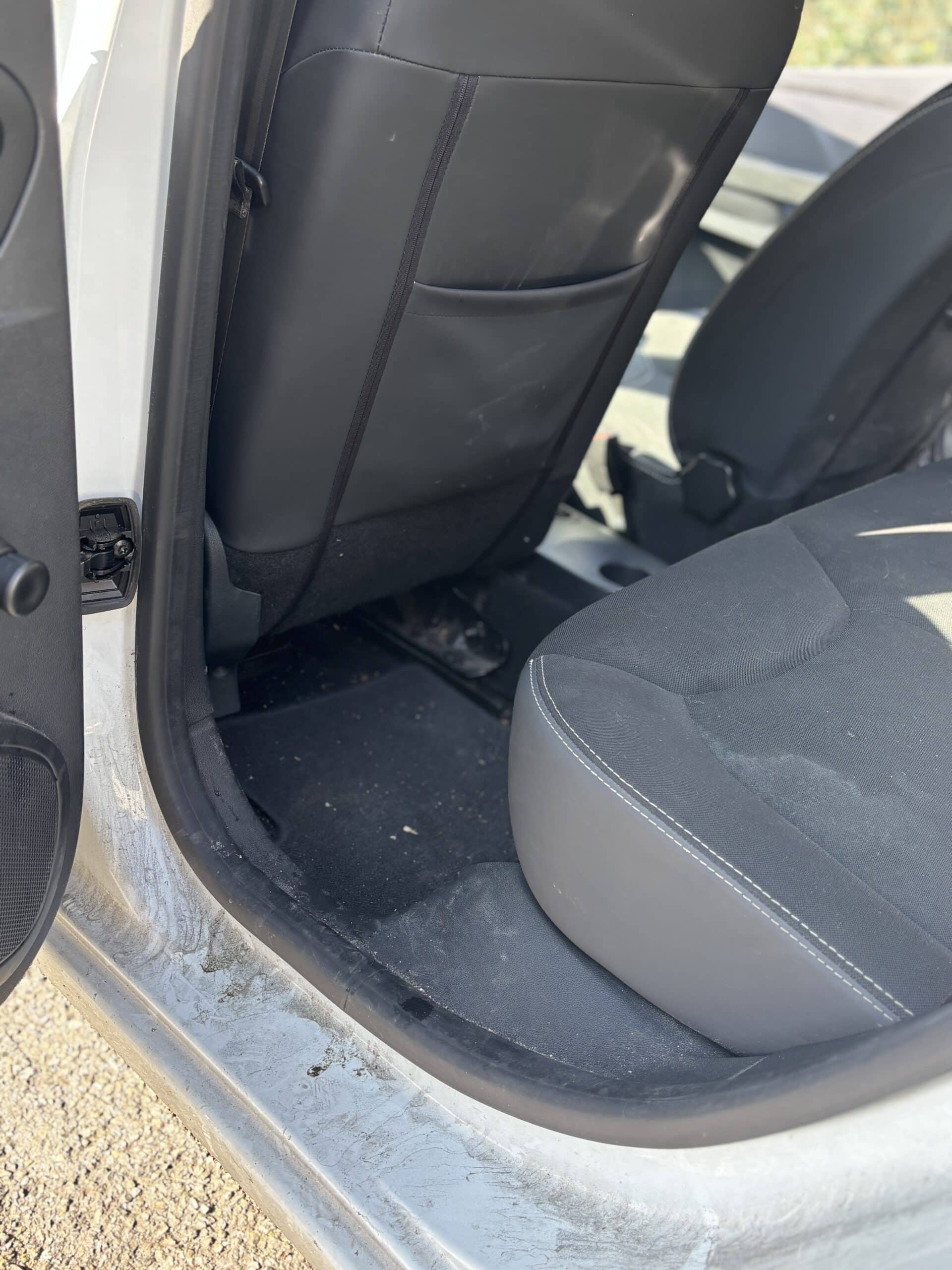 Intérieur de voiture blanche avec sièges noirs et tapis de sol sale nécessitant un nettoyage professionnel.