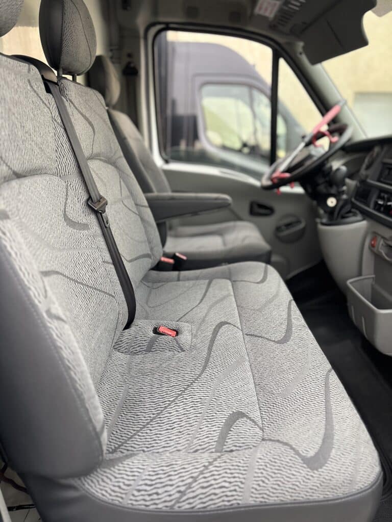 Sièges avant gris d'un utilitaire avec banquette double et ceinture de sécurité, vue intérieure de la cabine.