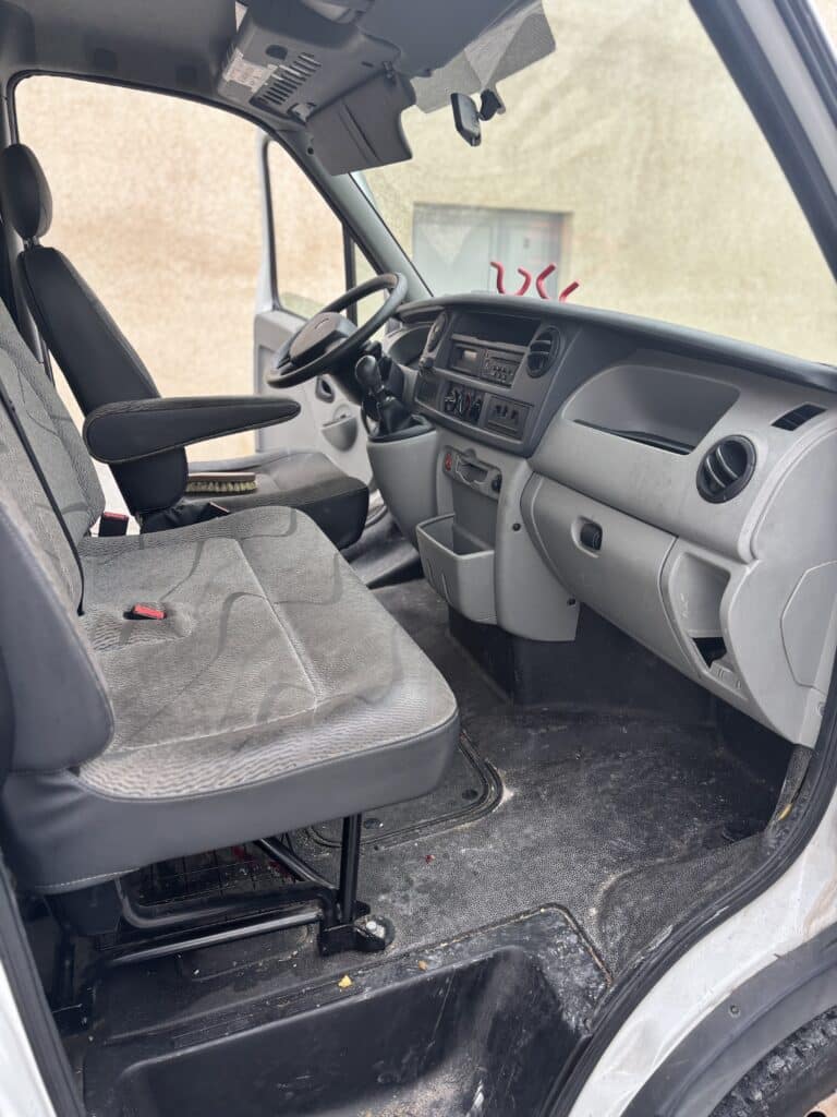 Cabine d'un fourgon utilitaire avec sièges en tissu gris et tableau de bord fonctionnel.