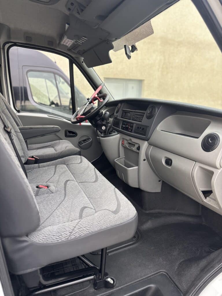Habitacle de camionnette avec sièges gris, volant muni d'un antivol rouge et tableau de bord ergonomique.