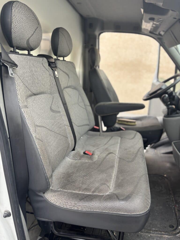 Sièges passagers gris d'un utilitaire avec motifs ondulés, ceintures de sécurité noires et vue sur le volant.