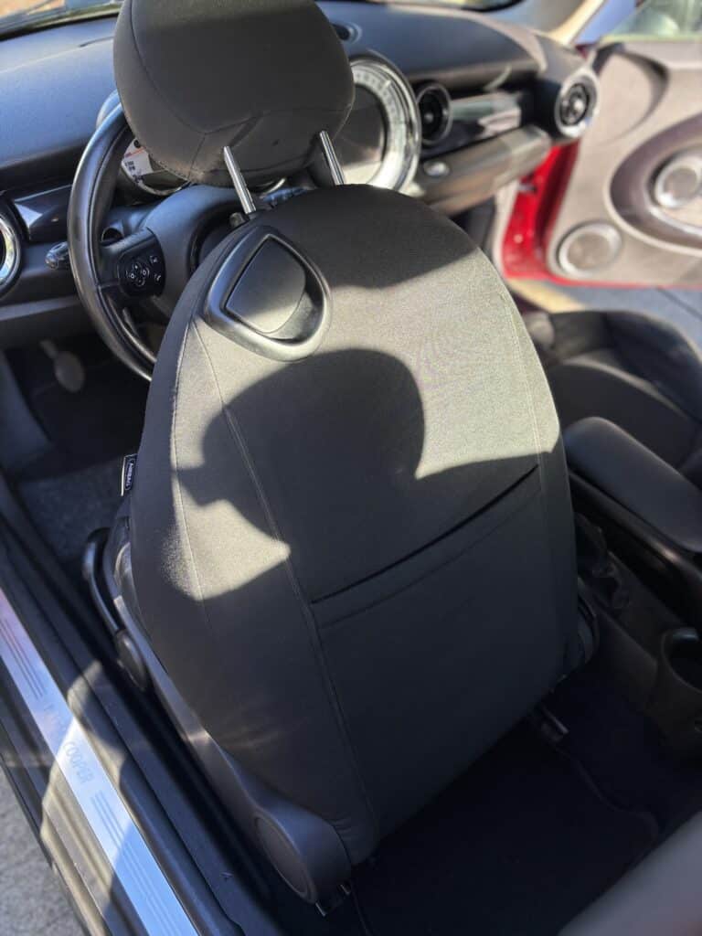 Intérieur de MINI Cooper avec siège conducteur en tissu noir, airbag latéral et seuil de porte marqué MINI COOPER.