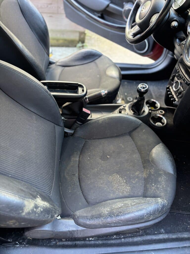 Sièges de Mini Cooper noirs avec taches de moisissure blanches sur le tissu et le cuir du côté conducteur.